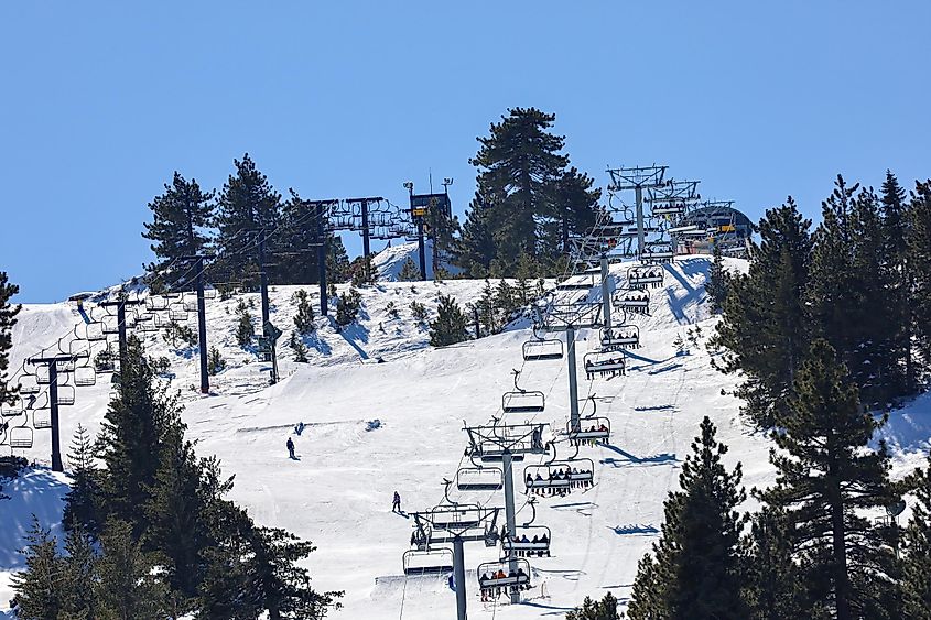 Snowed mountain slopes with people snowboarding and on the chairlifts at Snow Valley Ski Resort in Running Springs California.