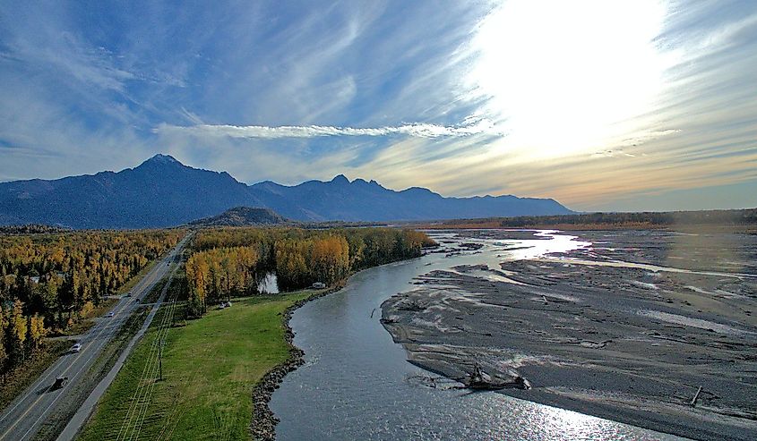 Aerial view of the Matanuska River surrounded by autumn trees against mountains in Palmer, Alaska