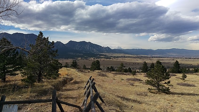 A hiking trail with wooden safety fence and nearby ponderosa pine trees frames a view of Colorado's Front Range. Broomfield, Colorado.