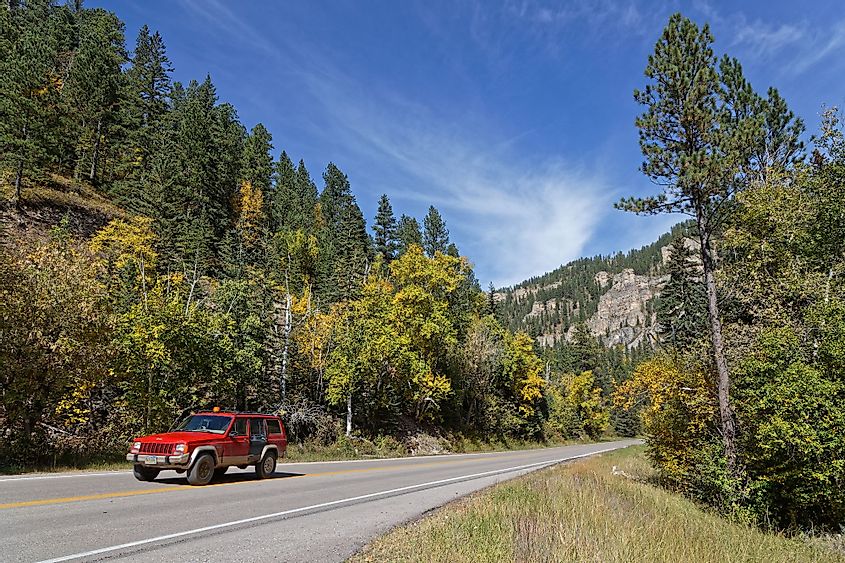 A red car drives in a fall landscape of Spearfish Canyon in Spearfish, South Dakota