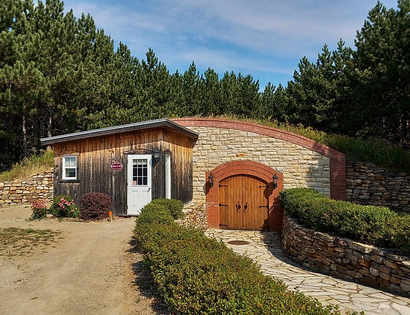 Editorial Photo Credit: Elsie Morand via Shutterstock. Saint-Gabriel Vineyard, Saint-Gabriel-de-Brandon, Quebec, Canada - April 9, 2021: Facade of a stone and wood wine barrel storage cellar.