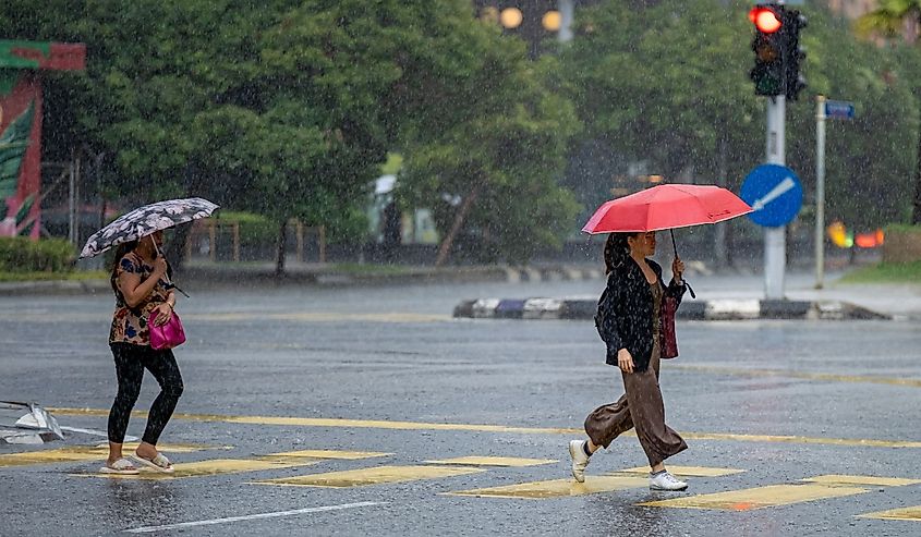 Women holding umbrellas while walking in heavy rain in Kuala Lumpur