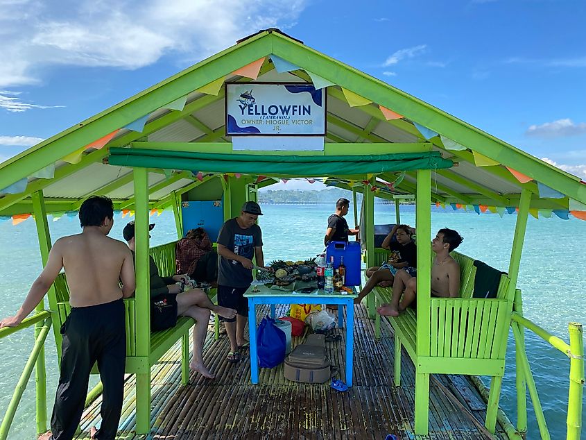 A Filipino family aboard a green floating dock making a meal of fresh fruit and fish.