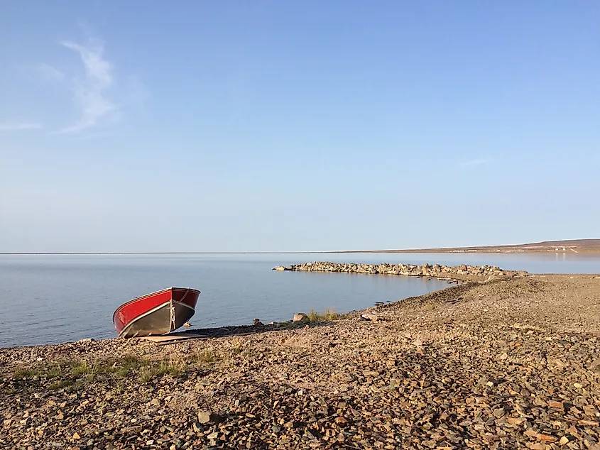 A small boat on a rocky lake shoreline under blue skies.