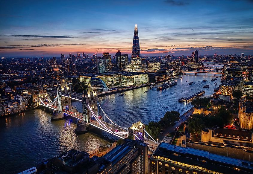 Elevated evening view of the illuminated skyline of London, England, with Tower Bridge and River Thames through the City lights