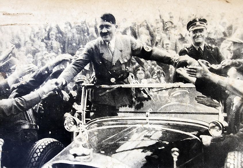Adolf Hitler stands in a convertible and shaking hands with his fans.