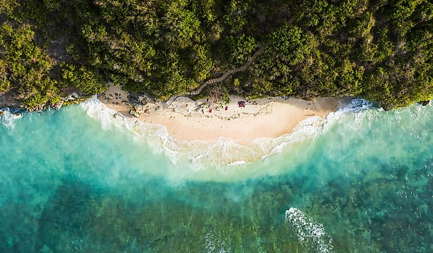 View from above, stunning aerial view of some tourists sunbathing on a beautiful beach bathed by a turquoise rough sea during sunset, Green Bowl Beach, South Bali, Indonesia.