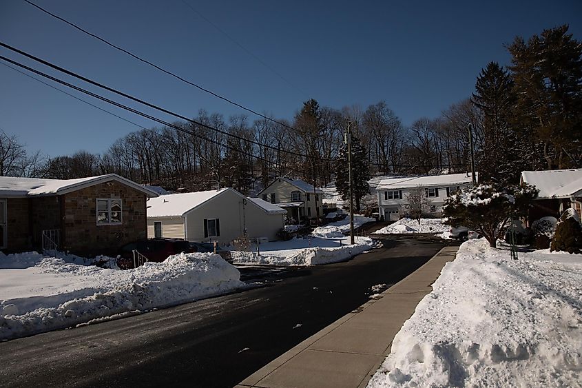 A typical American neighborhood is covered by snow, a road is plowed on a sunny bright day in Branford, Connecticut.