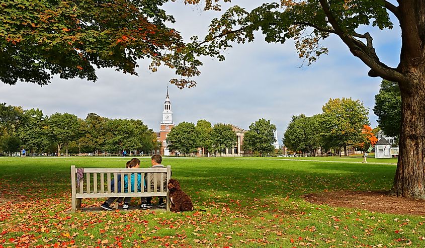 Two people sitting on a bench in front of the Baker-Berry Library on the campus of Dartmouth College with trees and green grass