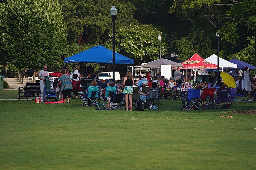 People gathered on a grassy lawn under colorful tents at an outdoor community event.