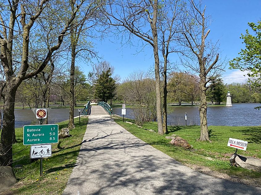 A signed paved path prepares to cross a pedestrian river bridge from one park to another.