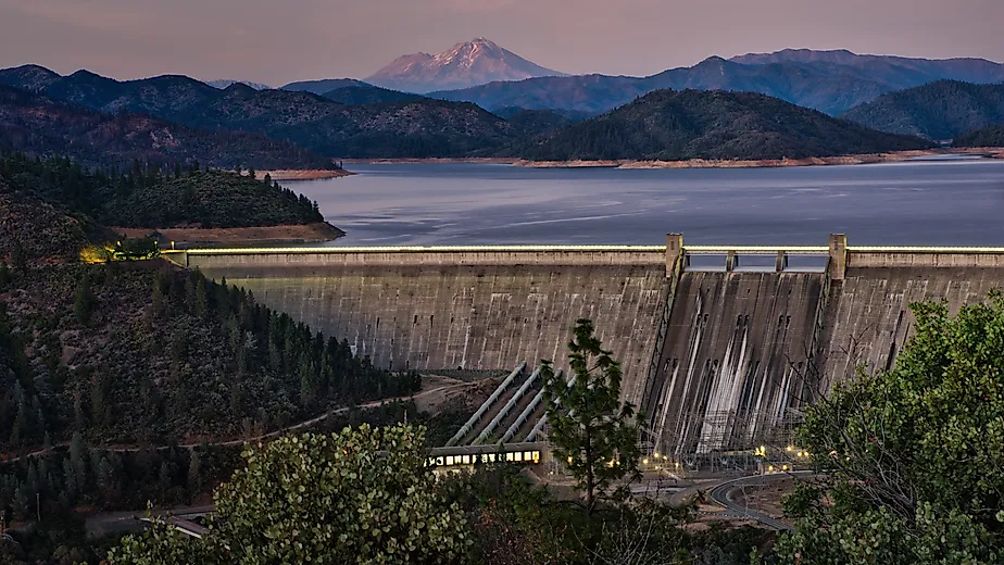 A picture of Shasta Dam with a lake and rocky mountains on the background during sunset. 