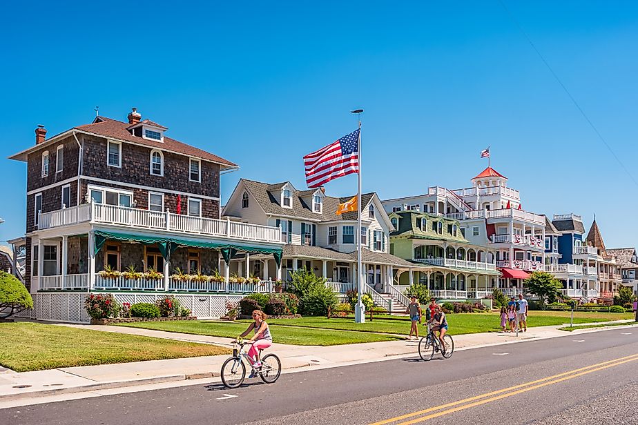 People bike and walk in front of traditional villas in Cape May, New Jersey, USA, on a sunny summer day.