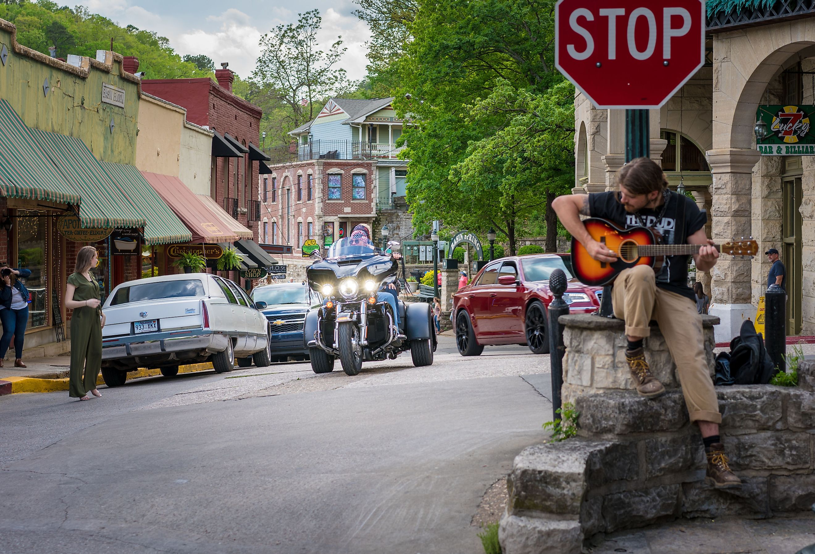 Man playing guitar at a stop sign, and cars and people on the street in downtown Eureka Springs, Arkansas. Image credit shuttersv via Shutterstock