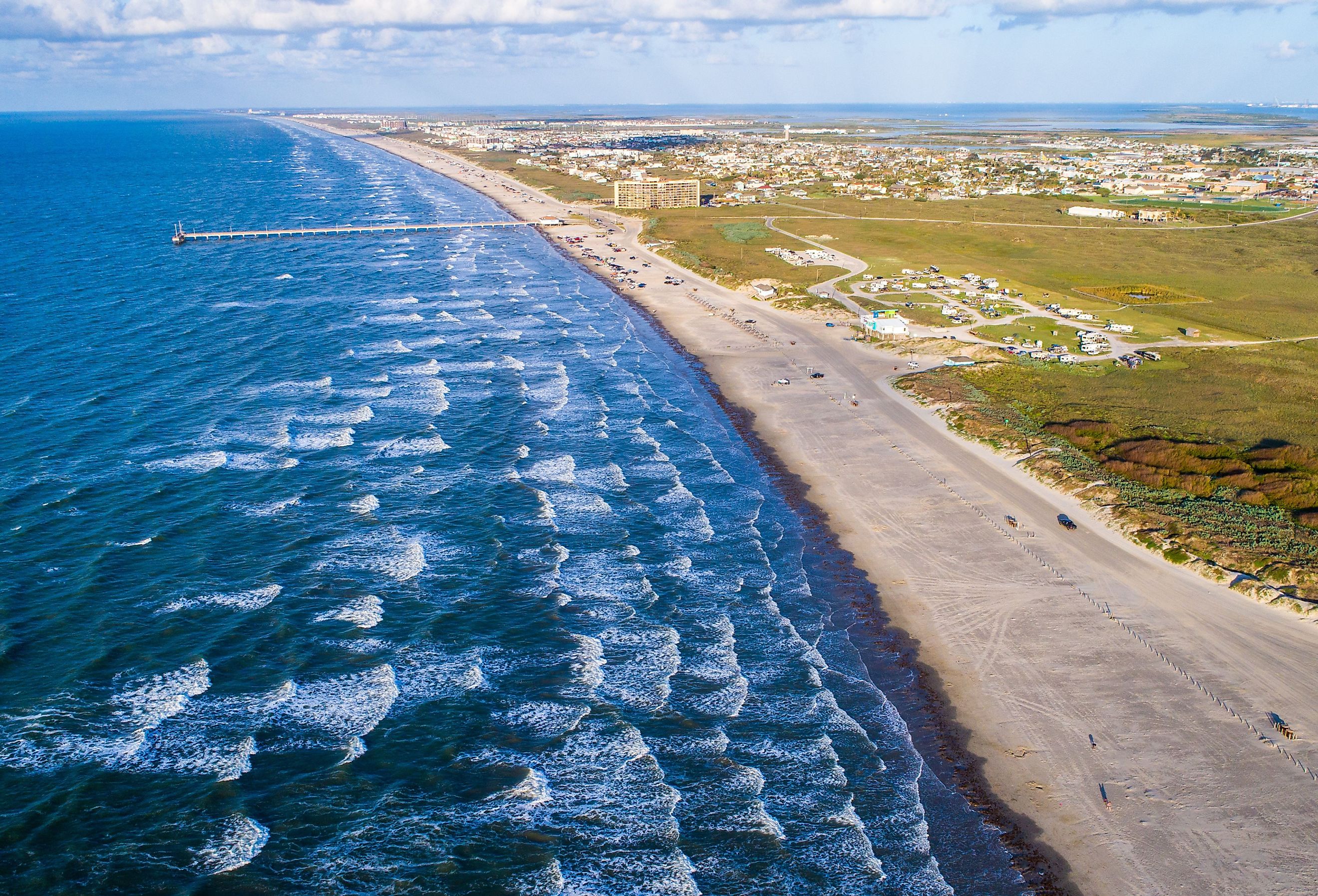 High above the Padre Island shoreline in Port Aransas, Texas waves crashing for miles with pier in the background deep blue water extended out into the Gulf of Mexico. Image credit Roschetzky Photography via Shutterstock.