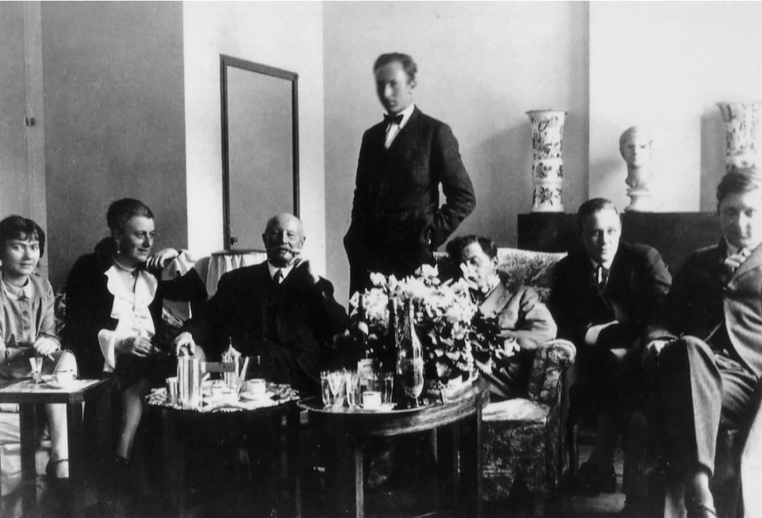 Ludwig Wittgenstein is sitting laughing with his friends, the sculpture he made sits at the back.