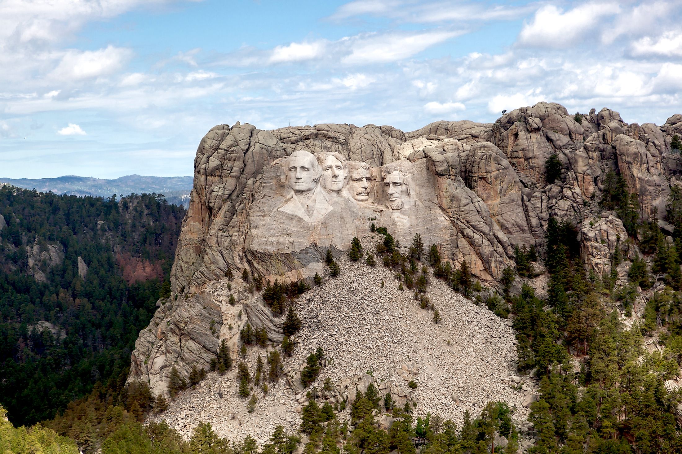 An aerial view of Mount Rushmore Narional Memorial showing the carved faces of past Presidents George Washington, Thomas Jefferson, Theodore Roosevelt, and Abraham Lincoln.