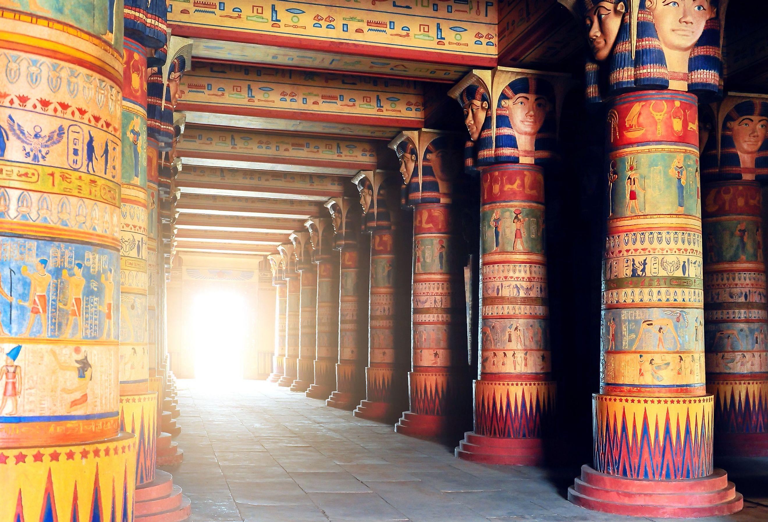 Colorful Ancient Egyptian writing on stone pillars in Egypt, lining a pathway to a bright entryway.