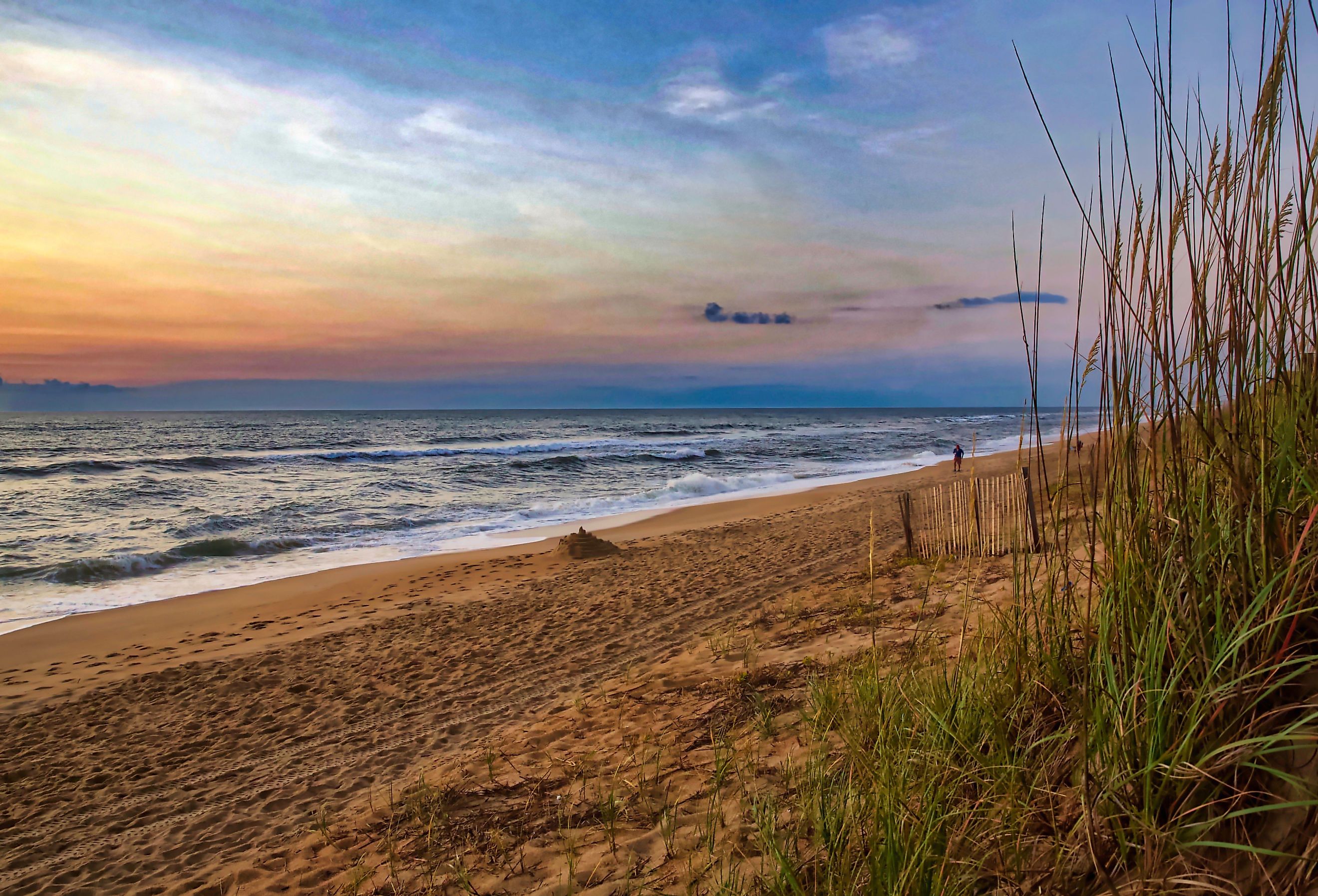 Colorful sunrise on a North Carolina beach, waves breaking on a sandy shore framed by dune grass. Duck, NC. Image credit Jeremy Tyree via Shutterstock. 