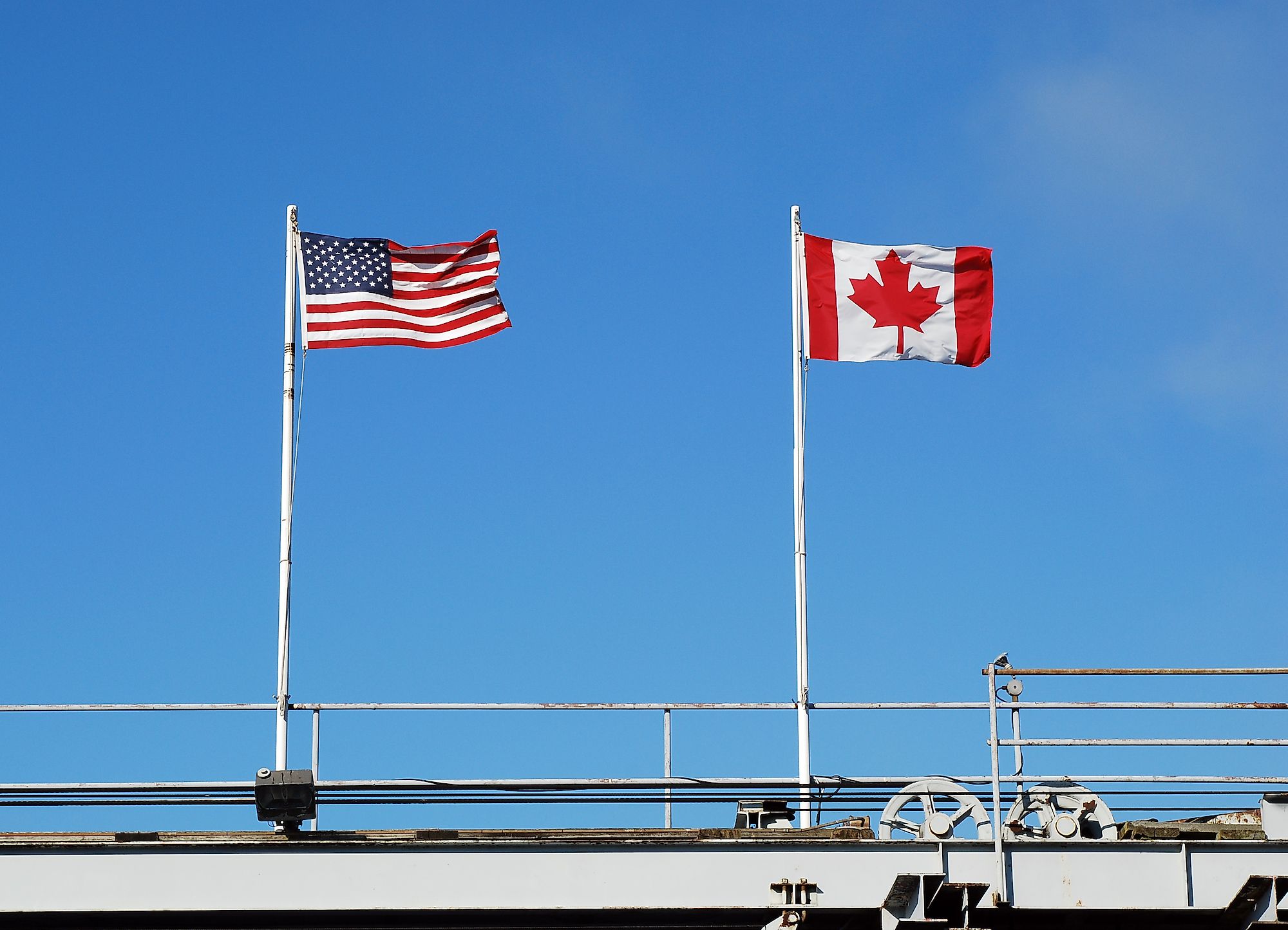 USA's and Canada's national flags fly at a US-Canada border. Image credit: Katherine Welles/Shutterstock.com