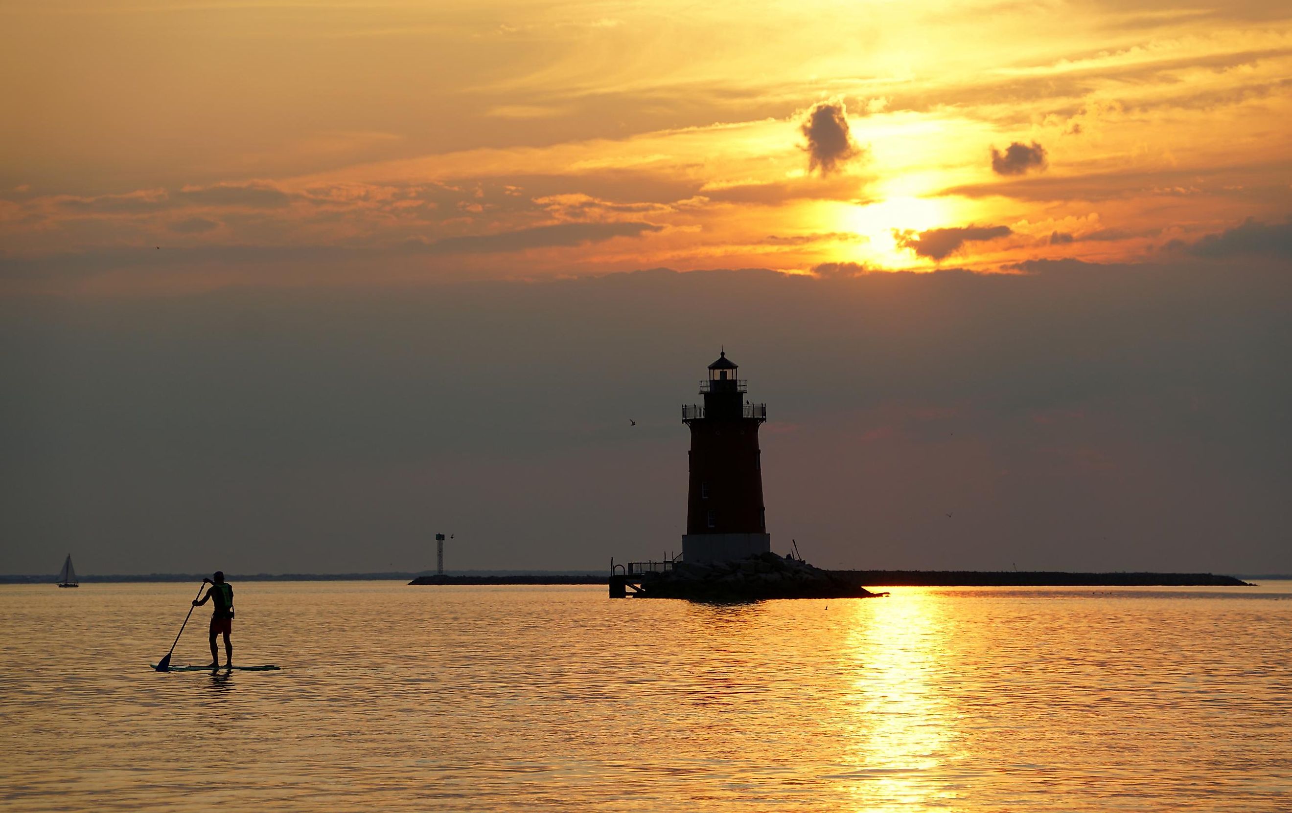 Silhouette of a light house and a man on a paddle board during sunset at Cape Henlopen State Park, Lewes, Delaware.