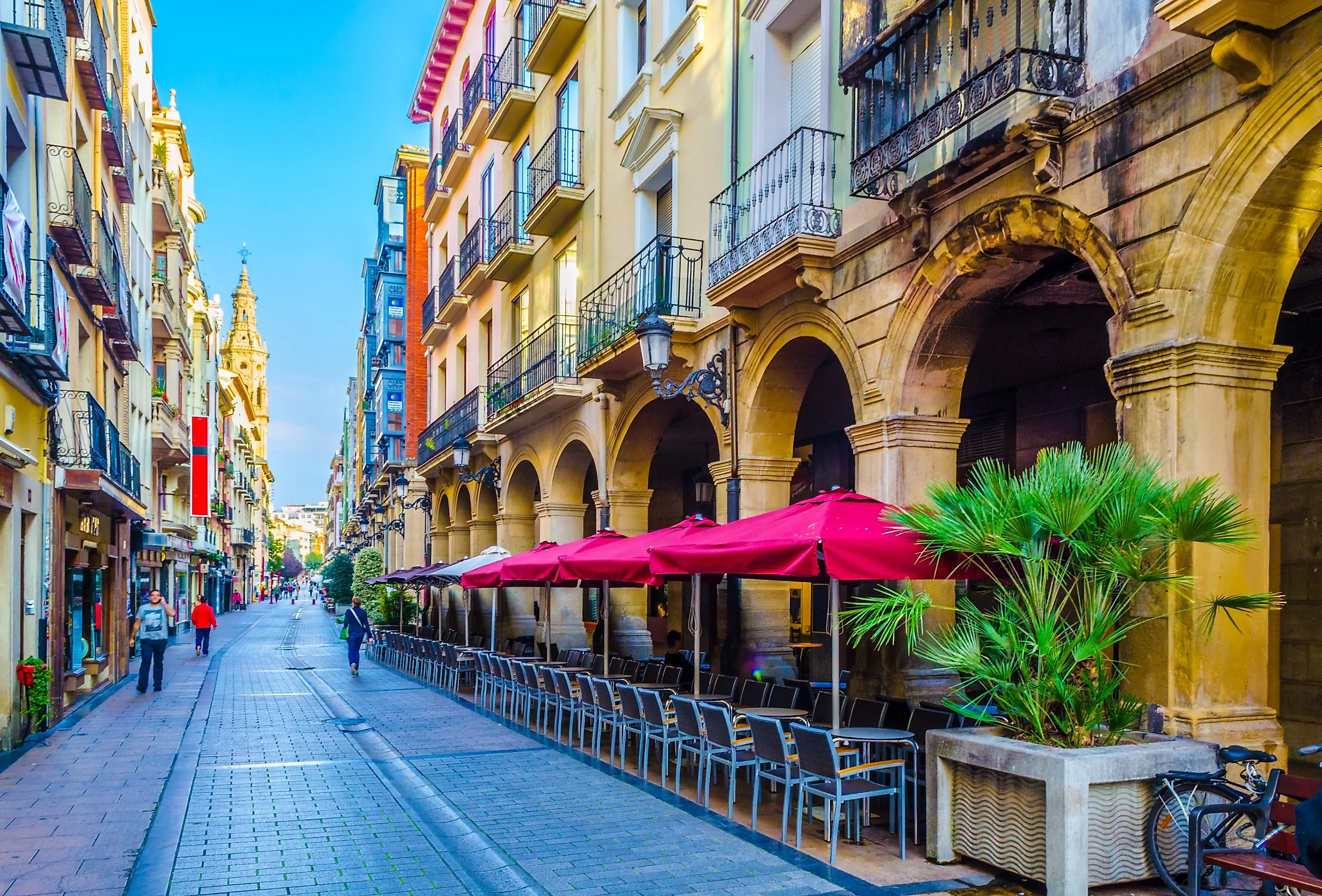 A crisp cobblestone street in Logroño, Spain. A long restaurant patio sits below lovely Juliet balconies, with the tall spire of an old church sprouting up in the background.