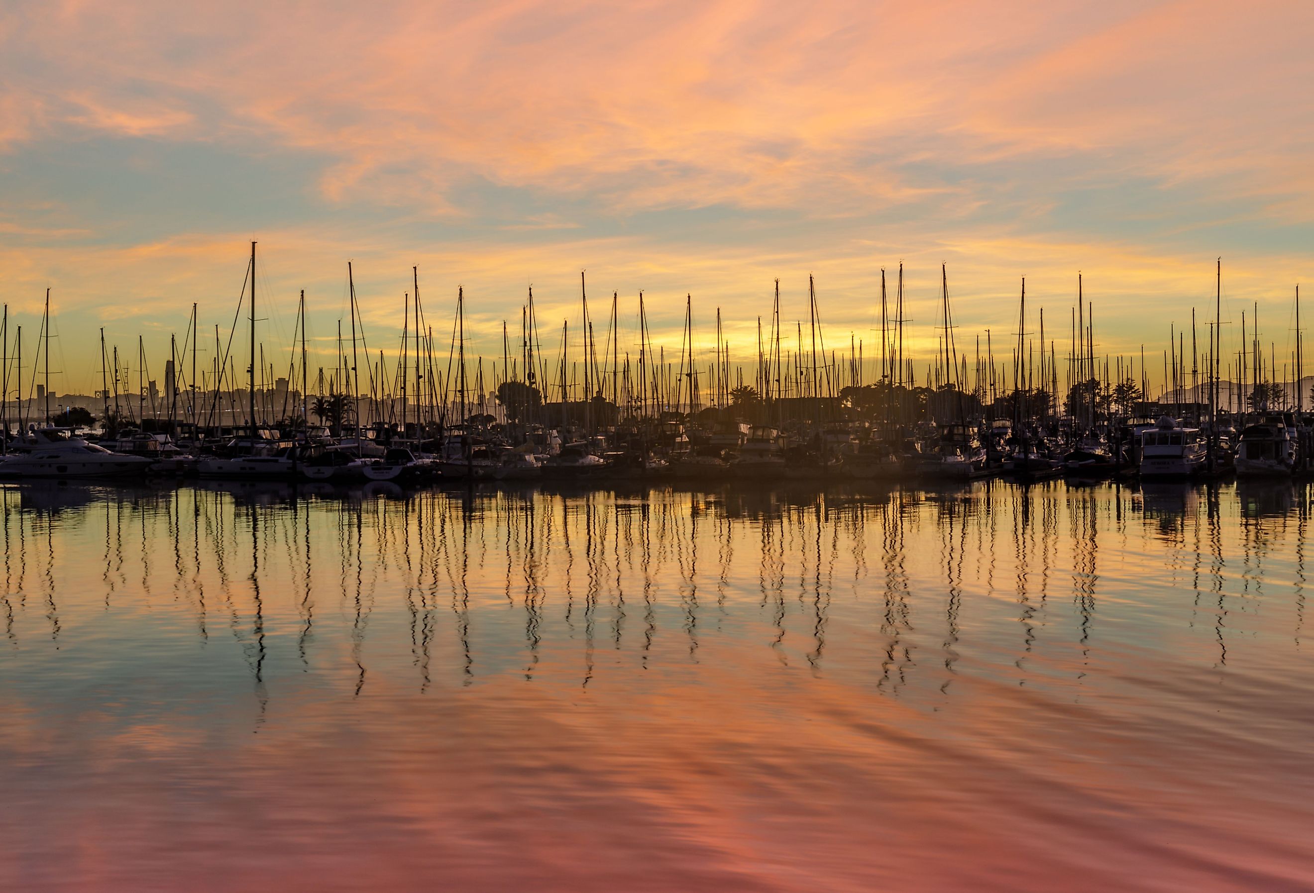 Sailboats moored in San Francisco Bay with sunset skies and water reflections in Alameda County. Image credit yhelfman via Shutterstock. 