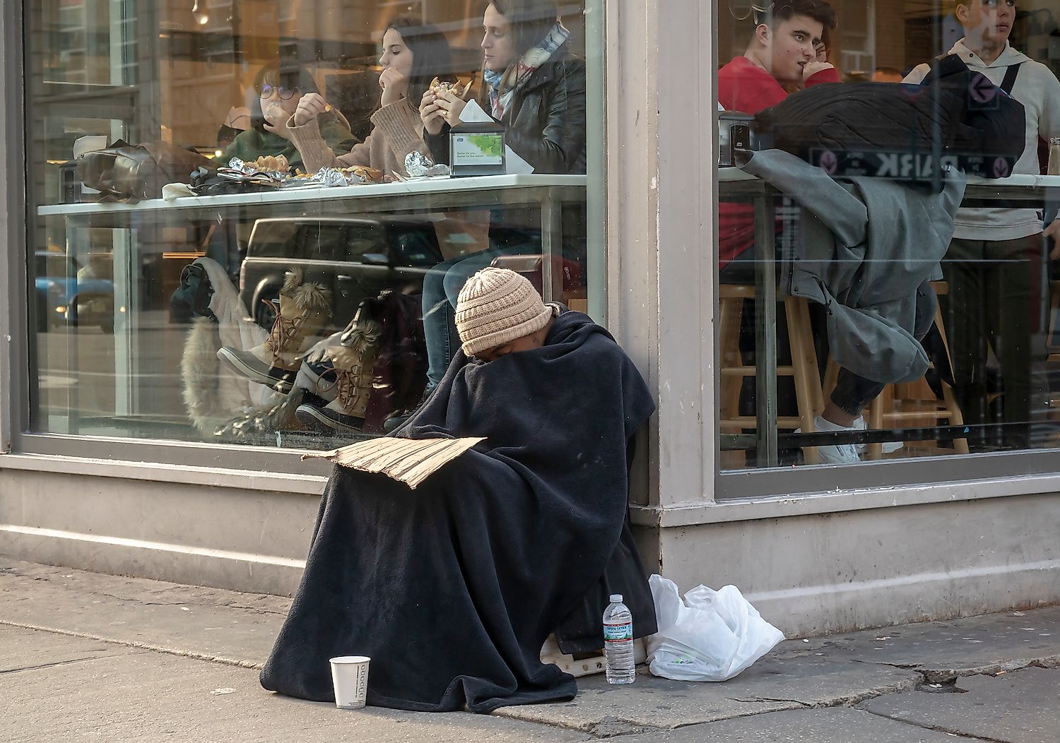 Homeless individual begs in front of a restaurant in the Chelsea neighborhood of New York. Image credit: Rblfmr/Shutterstock.com