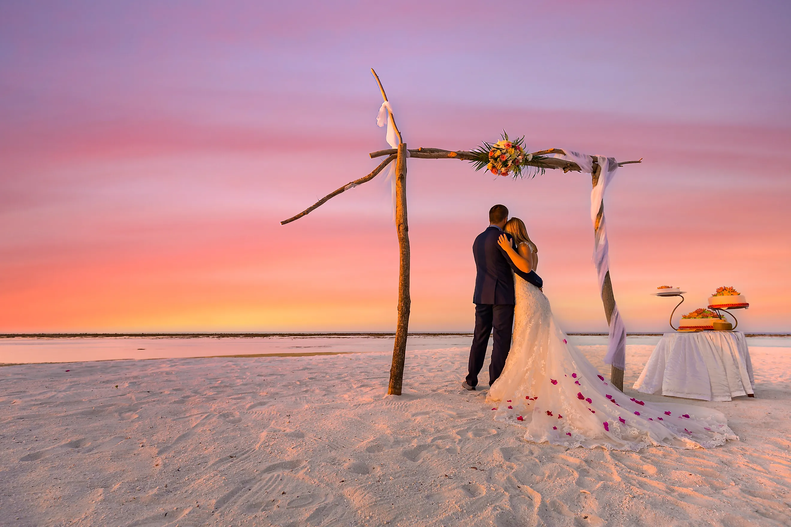 Bride and groom on the beach under wedding arch with cake.