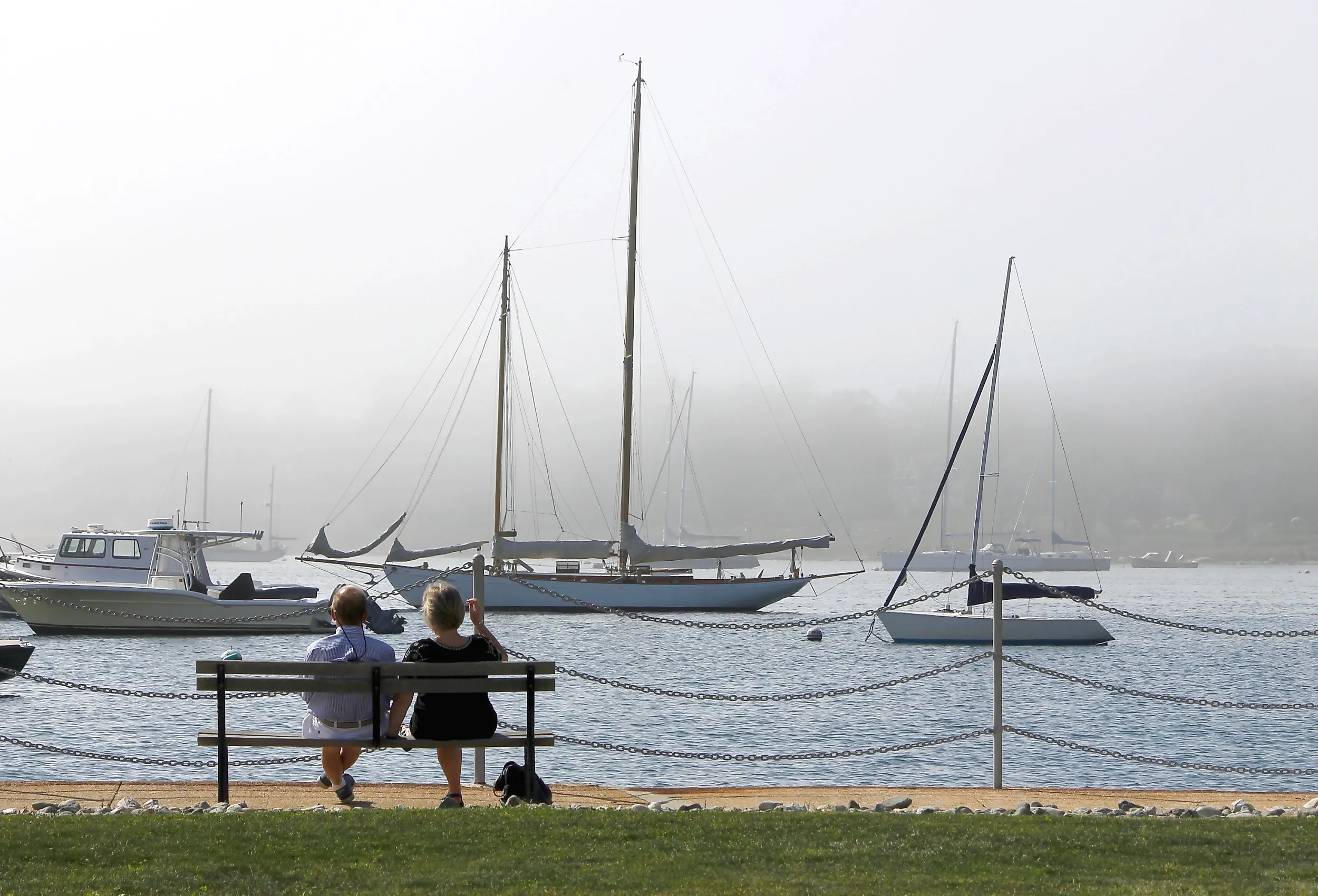 Couple on a bench looks out over a foggy harbor full of boats in Stonington. Image credit: TheBrassGlass via Shutterstock.
