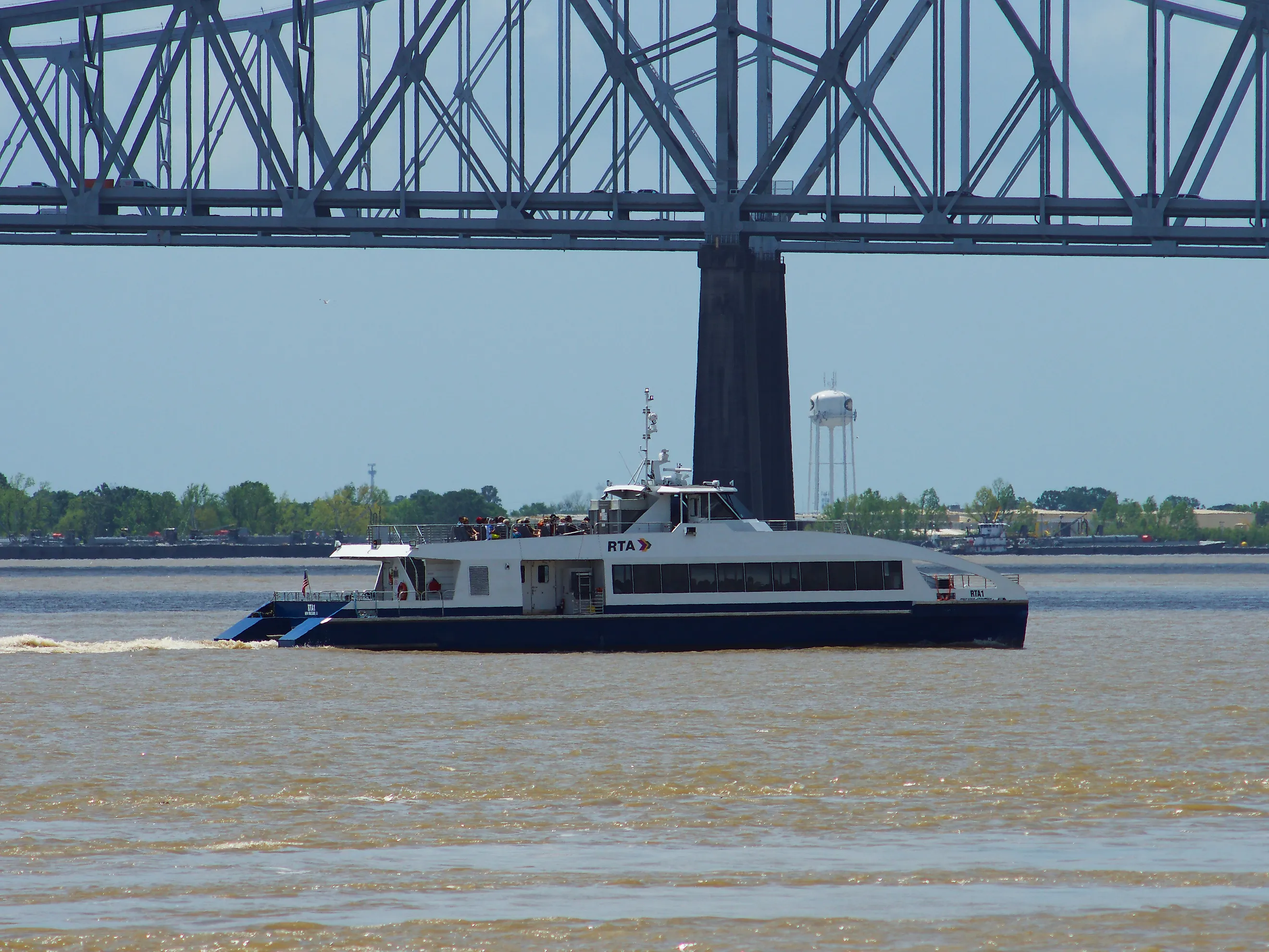 A ferry crosses the Mississippi River under a bridge in New Orleans, via Wirestock on iStock.com