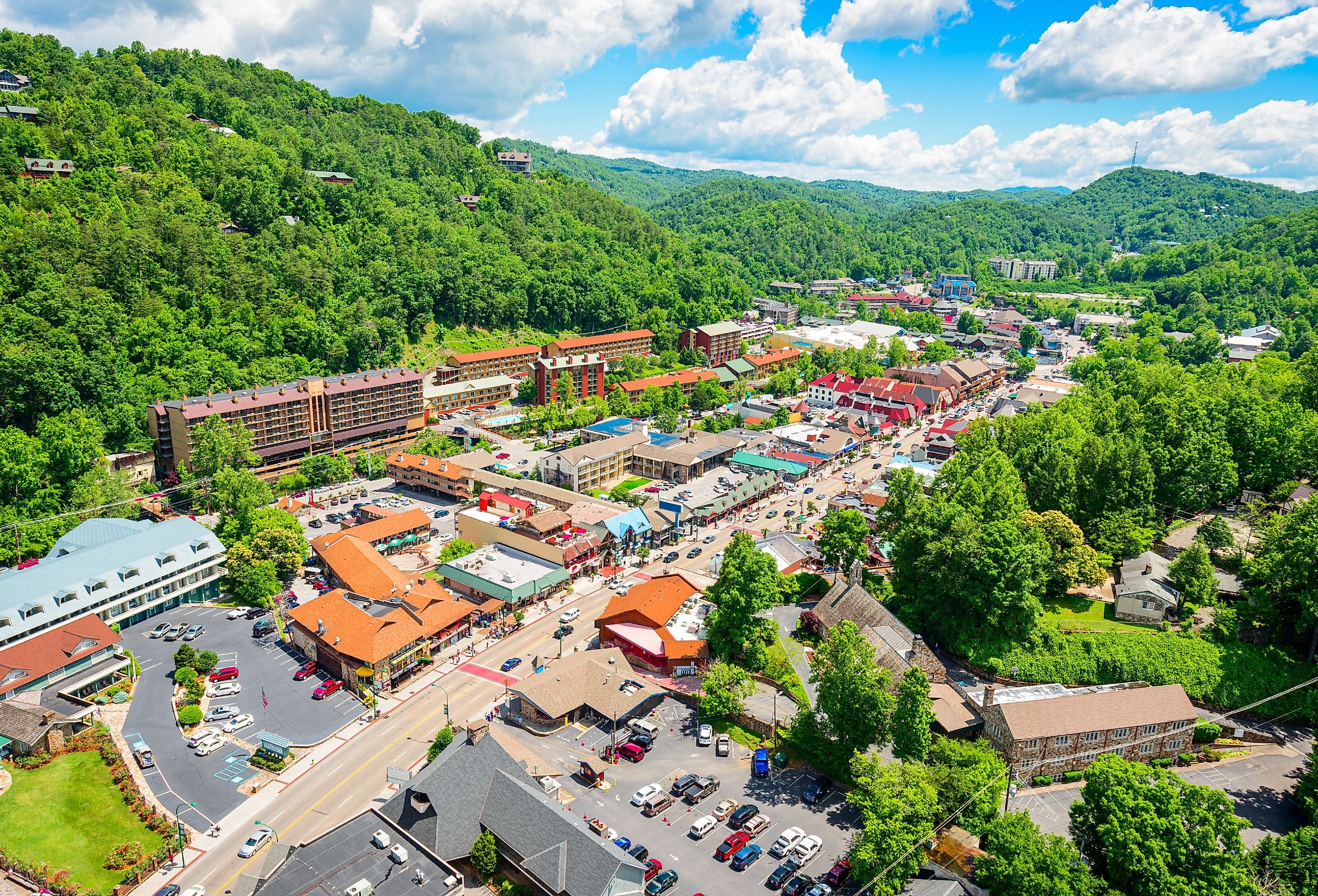 Aerial view of Gatlinburg, Tennessee surrounded by trees and mountains on a sunny day.
