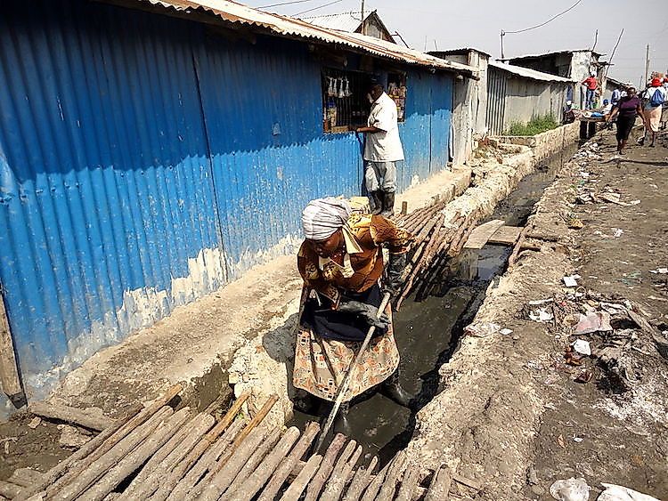 A woman cleaning drainage ditches in Kenya to discourage mosquito breeding and thus prevent malaria.