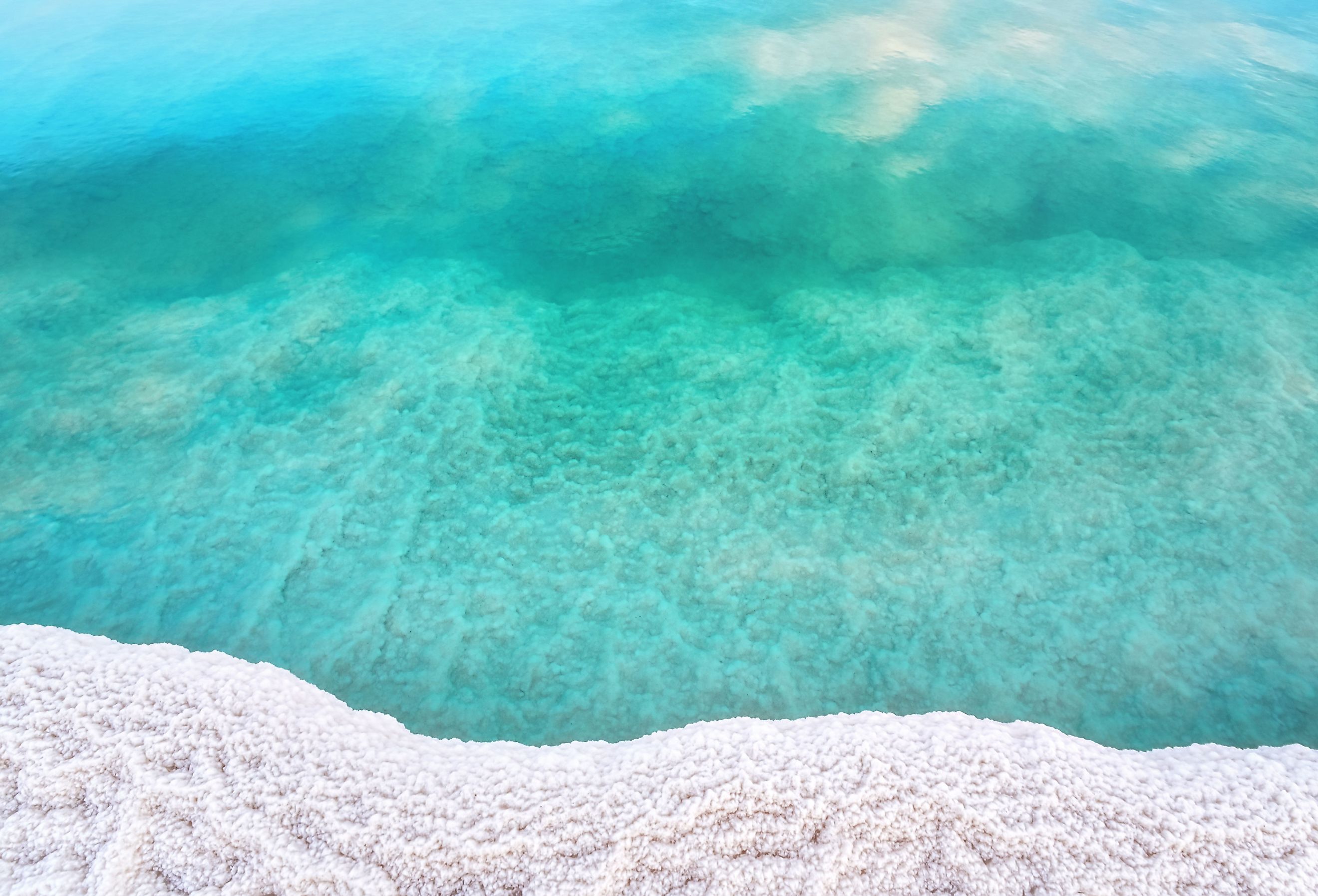 Shore of Dead sea in Ein Bokek, Israel, white salt crystals outside and at the bottom, turquoise clear water.