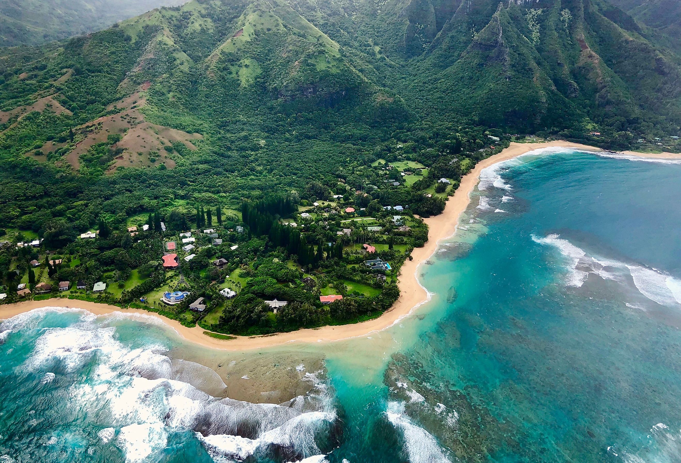 Homes along the sandy coast with mountains towering in the background in Hanapepe, Kauai, Hawaii.