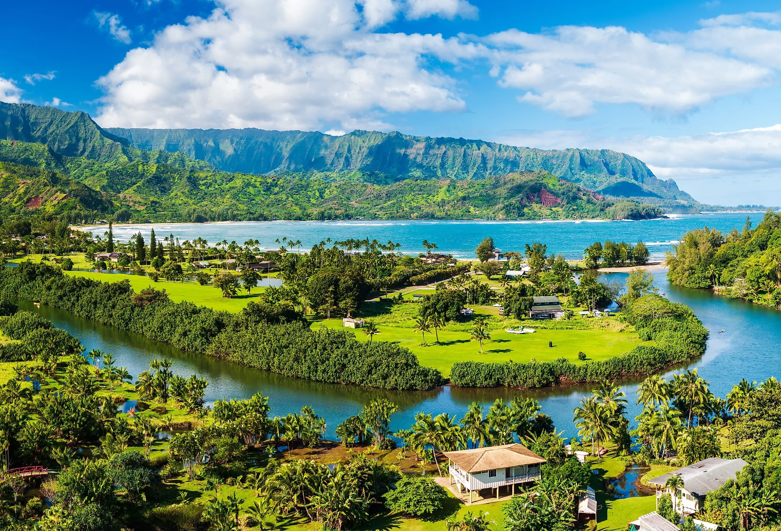 A vibrant aerial view of the lush landscape of Hanalei Bay, framed by majestic mountains under a sunny, blue sky in Kauai, Hawaii.