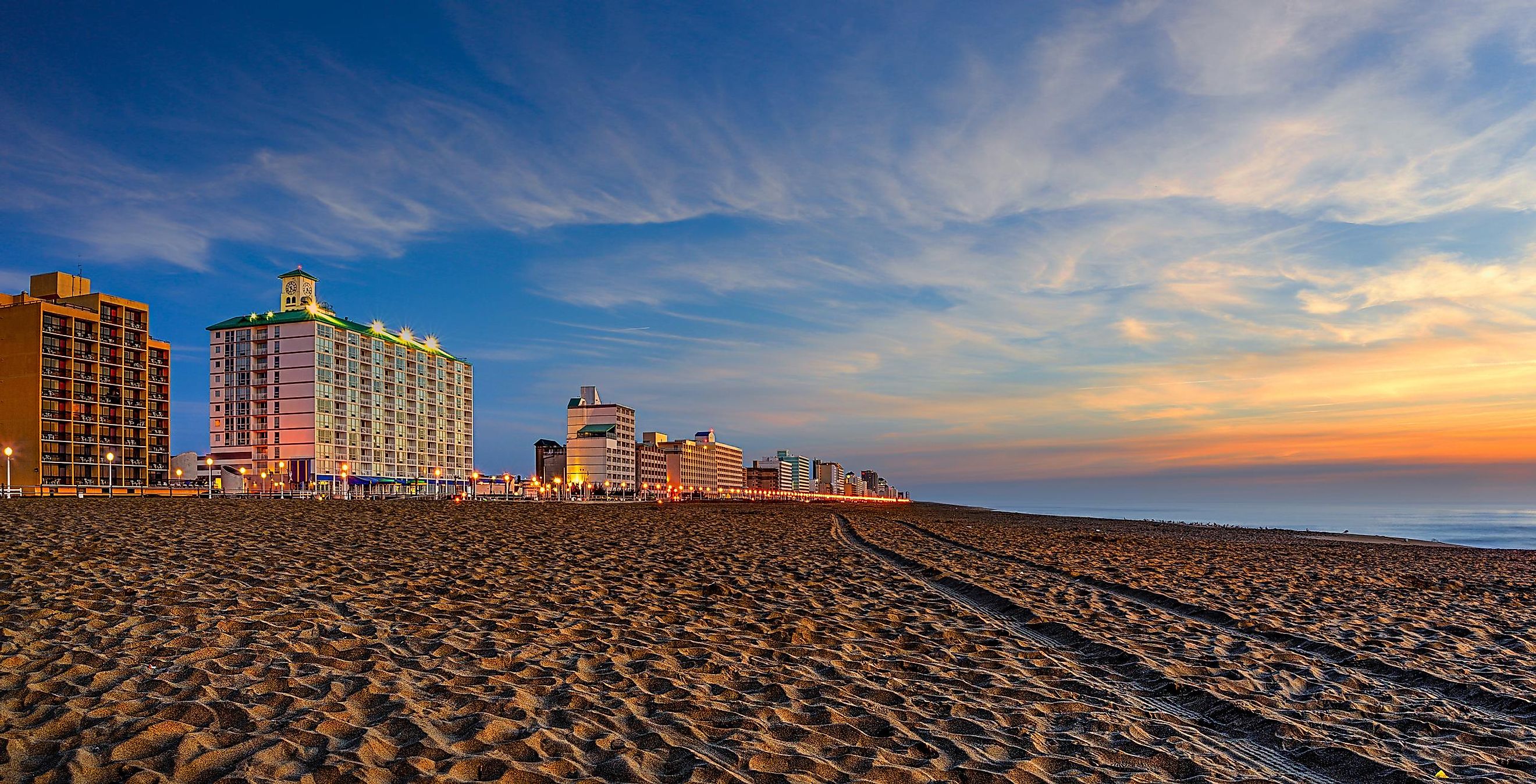 Virginia Beach, Virginia at sunset with lights on the boardwalk and buildings in the background. Image credit jomo333 via AdobeStock.