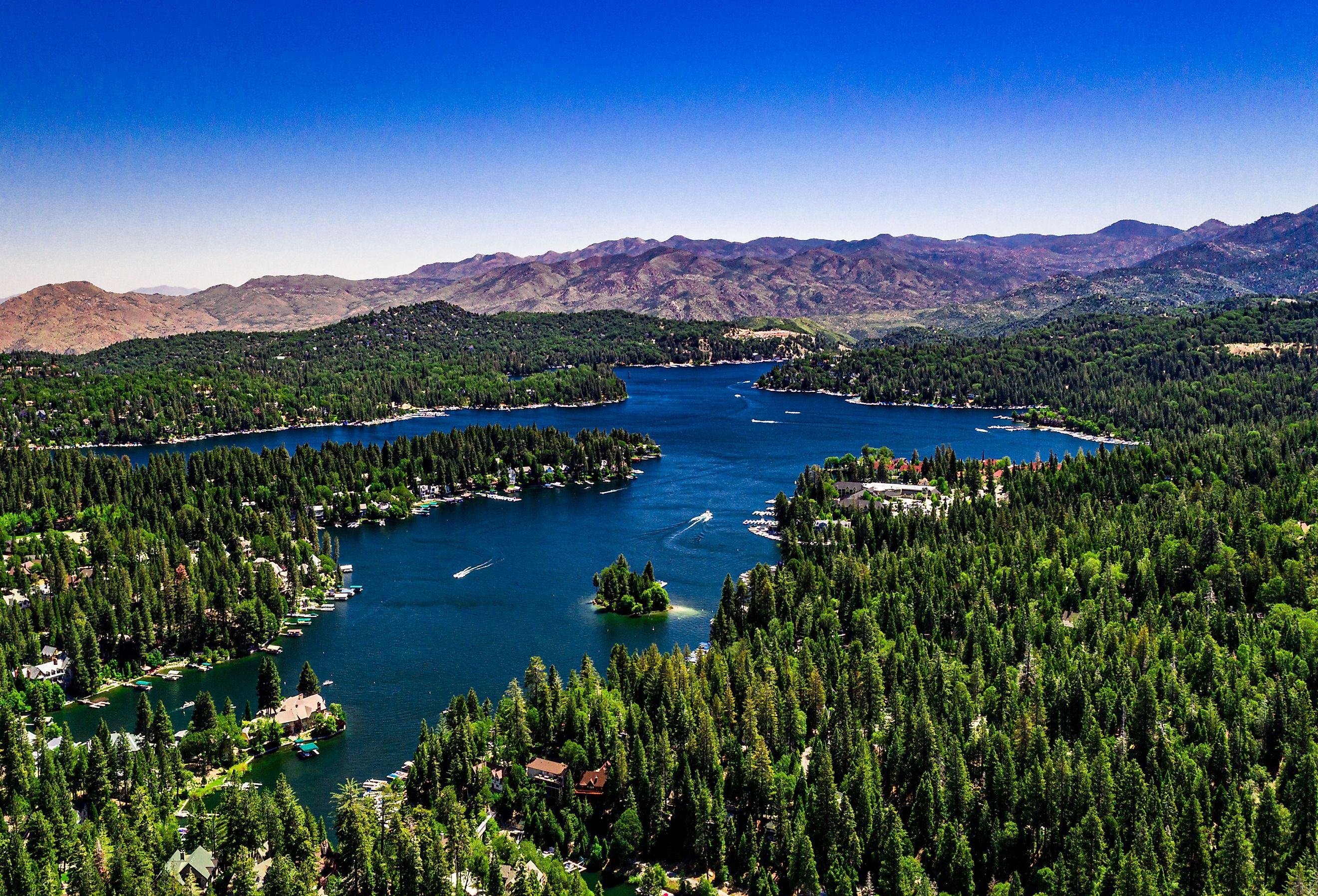 Aerial, drone panorama of Lake Arrowhead in the San Bernardino Mountains, California on a clear, summer day with blue water and sky, purple mountains and green trees