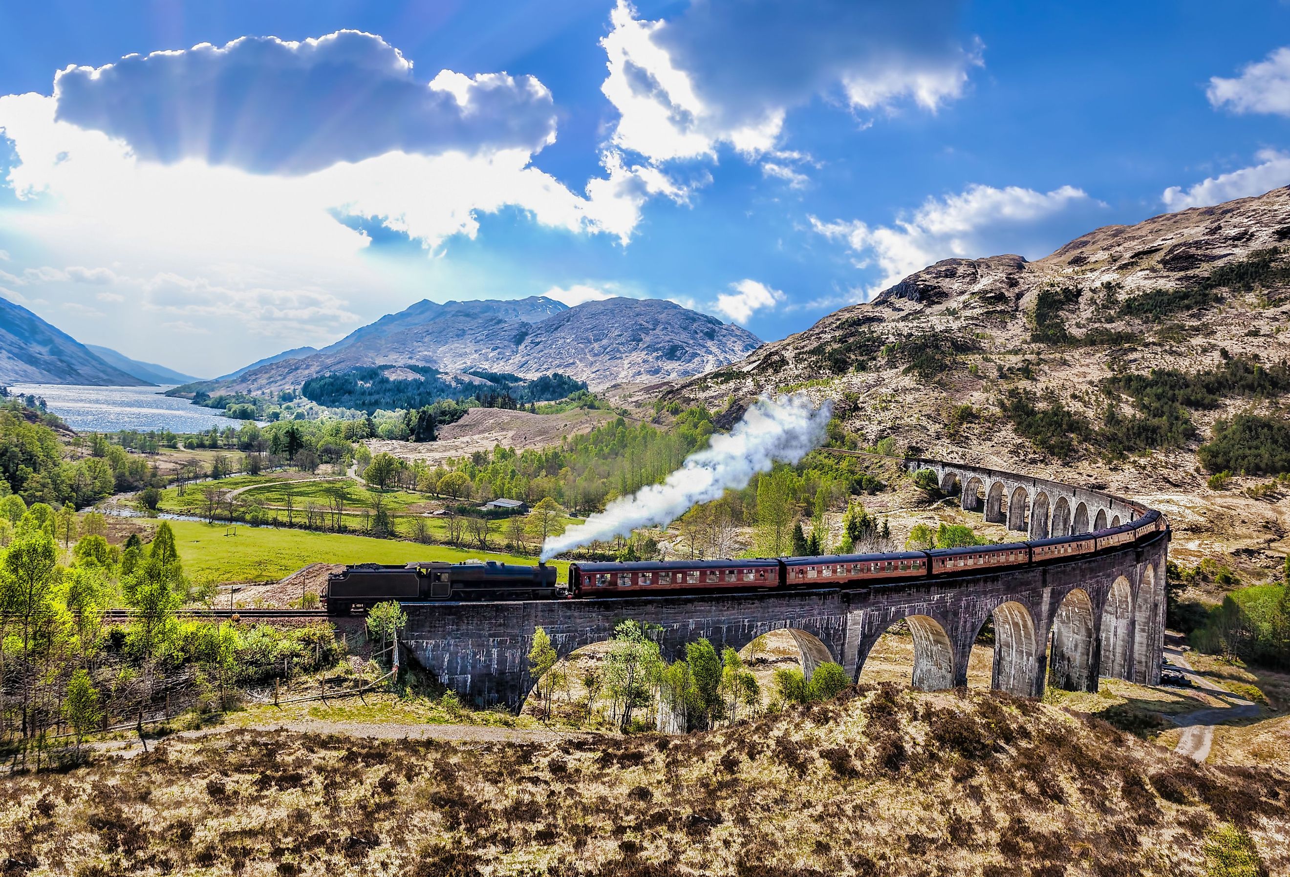 Glenfinnan Railway Viaduct in Scotland with the Jacobite steam train against sunset over lake. Image credit: Tomas Marek via Shutterstock