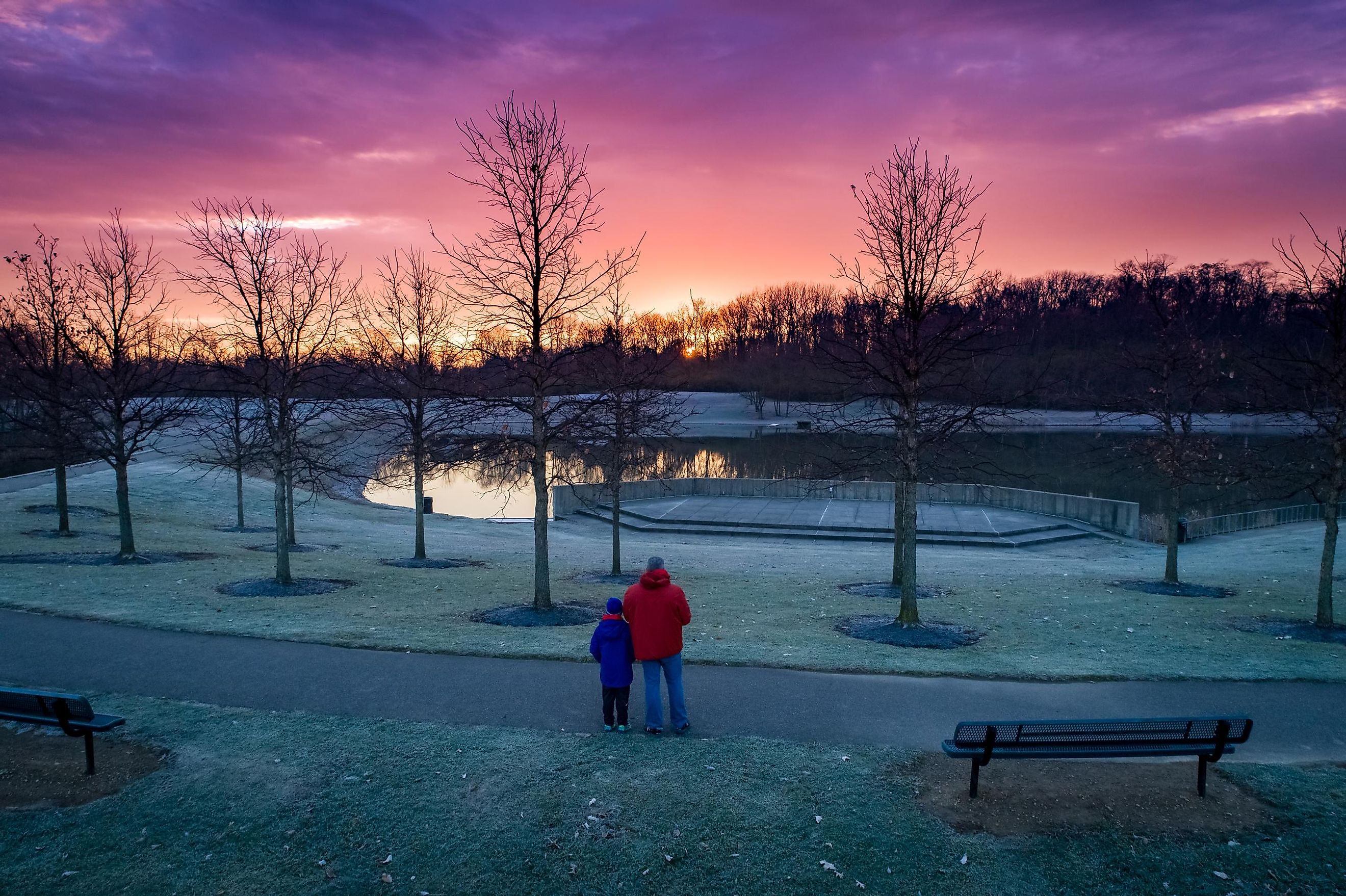 Aerial view from a drone capturing a father and son admiring the sunrise over the trees and lake at the park in Beavercreek, Ohio.