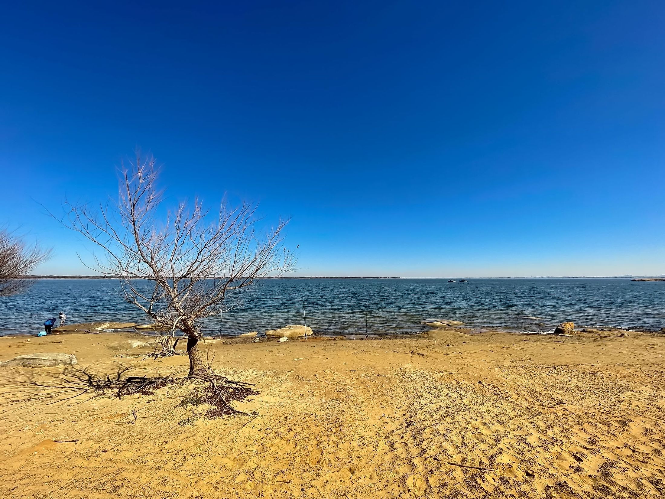 Unidentified children in winter jacket playing along the sandy rocky shoreline of Lake Lewisville during winter. 