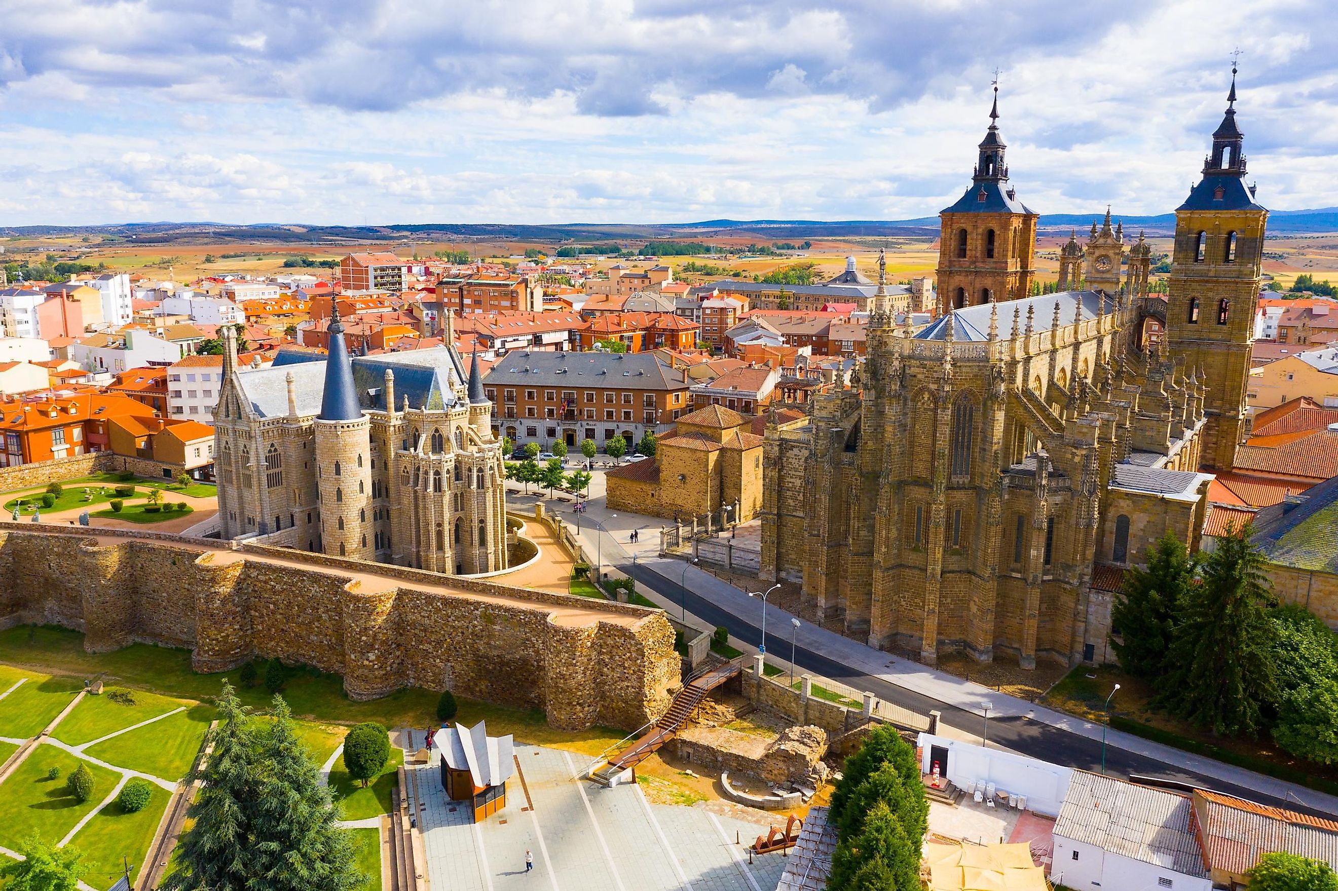 A massive Spanish cathedral (Santa Maria Cathedral) stands to the right of the quirky Episcopal Palace designed by Antonio Gaudi. The town of Astorga resides in the backdrop, as does the wide open Northwestern Spanish countryside. Clouds loom overhead.
