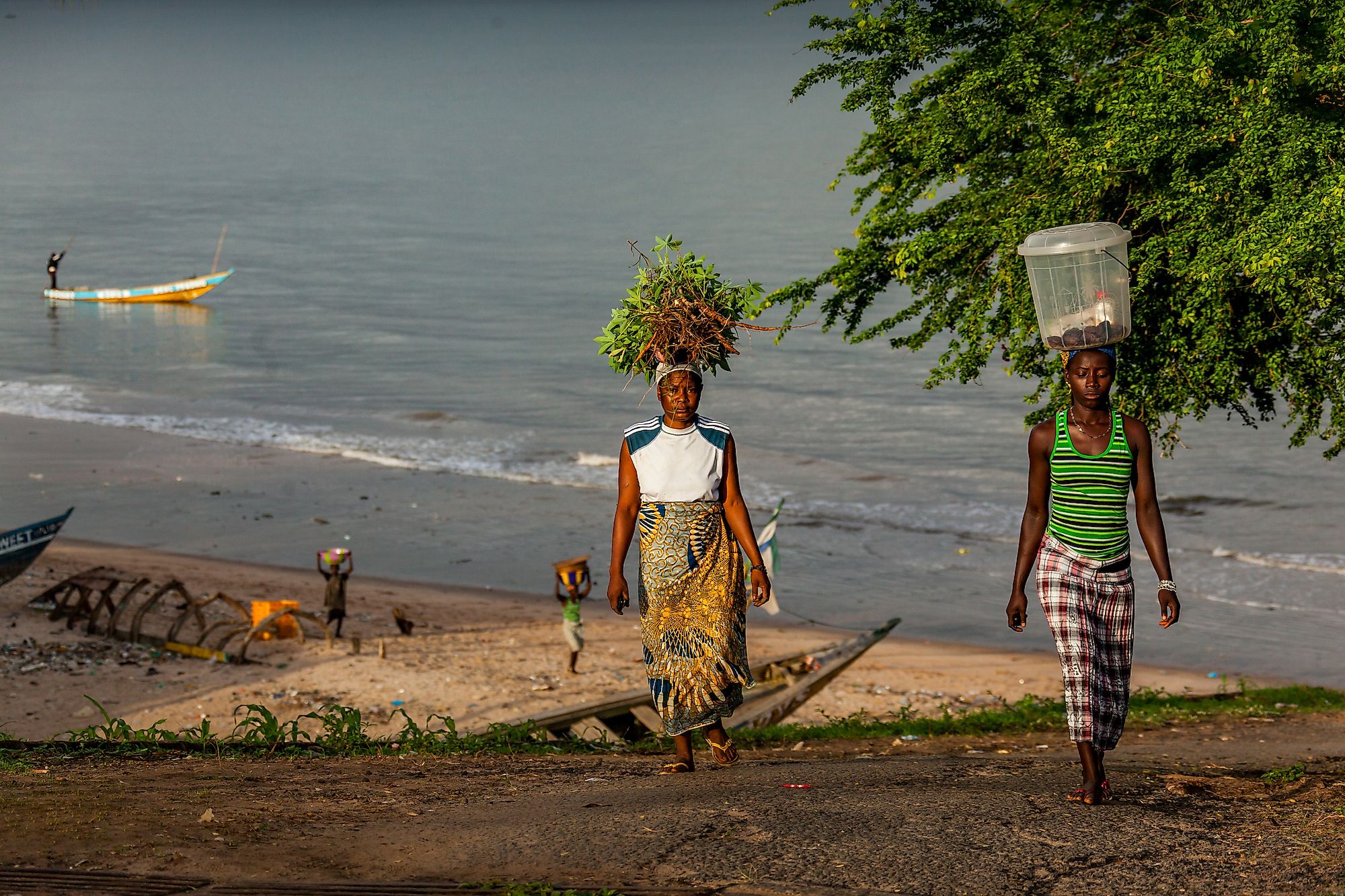 Two people with vegetables on head along a beach in Yongoro, Sierra Leone. Image credit: robertonencini/Shutterstock.com.