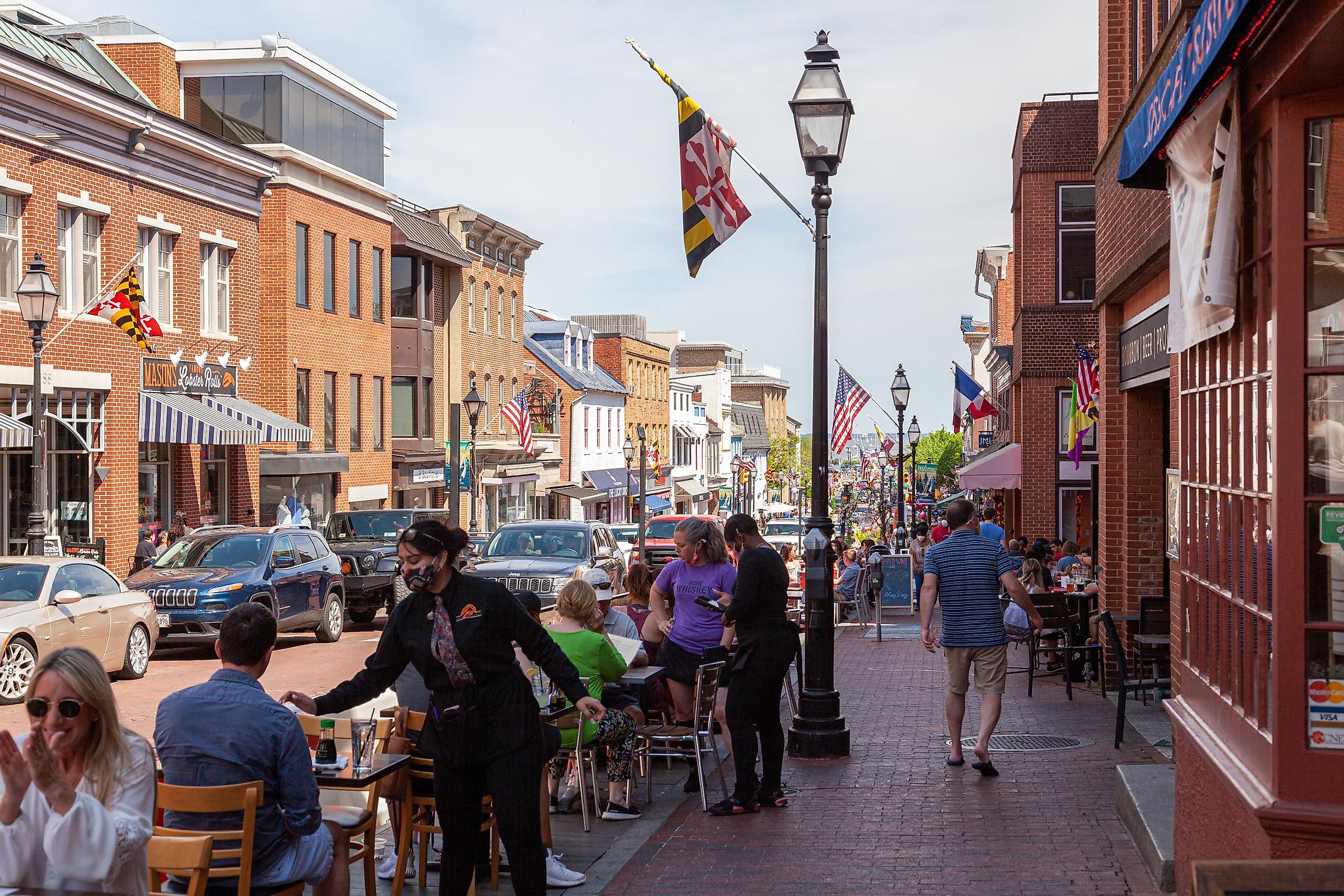 Street view of Annapolis, Maryland, with people walking in the historic town and people dining outdoors. Editorial Credit: grandbrothers via Shutterstock.