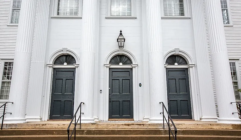 Front of Cheshire town church building with staircase and three black doors with transoms and tall white column pillars